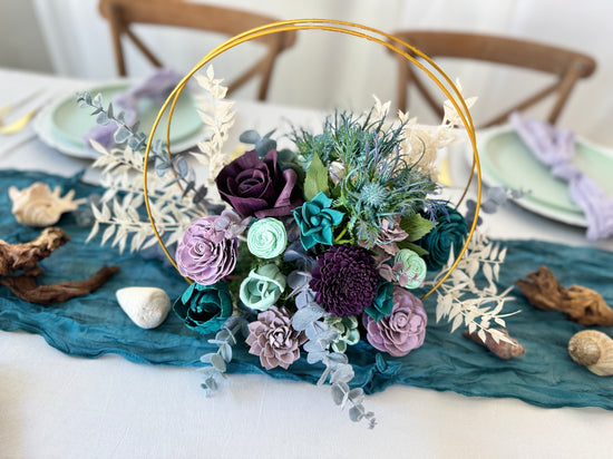 Whimsical Double hoop wedding centerpiece arrangement with teal, deep purple and lilac flowers. Adorned with sea thistle